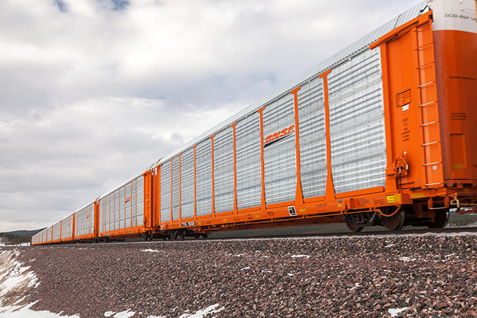 Auto rack train rolls through plains with mountain range in distance. Auto rack train rolls through plains with mountain range in distance.